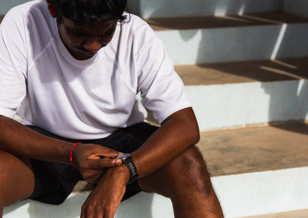Close up Asian young athlete sport runner black man wear modern time smart watch he sitting resting before training running at the outdoor street health park, healthy exercise before workout conceptの写真素材