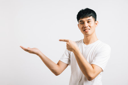 Portrait of a smiling, happy man pointing his finger to the side with confidence. Asian young man in a studio shot isolated on white, providing copy space.の写真素材