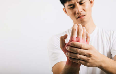 A man in pain, with a portrait showing palm and hand discomfort, massages his sore hands. Studio shot isolated on white background, illustrating health care and the concept of arthritis.の写真素材
