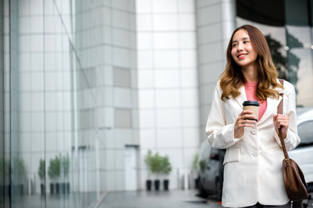 Portrait of confidence Asian businesswoman looking away and holding brown bag and having coffee cup. She successfully work go to against city scene in background of modern office buildings.の写真素材