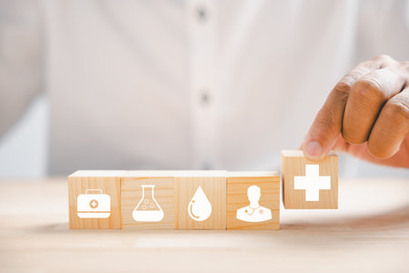Wooden block with healthcare and medical icons held by hand signifies safety, health, and family well-being. Symbolic of pharmacy, heart care, and happiness. health care conceptの写真素材