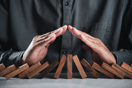 Business man holding hand upper to prevent protect domino wood block like risk, Hands of businessman cover protecting roof over wooden team, Risk assessment and managementの写真素材