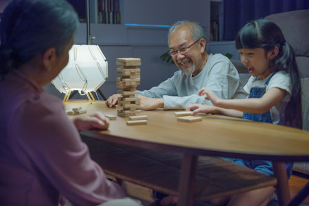 Happy grandparents Asian family enjoy playing toy block with little daughter and mother together at home night time, Smiling parent having fun play build constructor tower of wooden blocks, educationの写真素材
