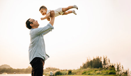 Playful family moment, father holds happy little boy up high, throwing up in sky on his birthday. cheerful child enjoys moment of freedom and joy, while the loving dad captures precious memory foreverの写真素材