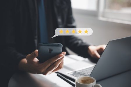 Positive feedback is a valuable business asset. A mans hand using a smartphone and laptop computer with a 5-star popup for satisfaction survey and performance evaluationの写真素材