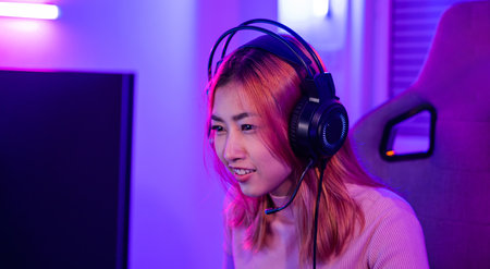 Happy Gamer endeavor plays online video games tournament with computer neon lights, young woman wearing gaming headphones intend to do playing live stream games online at homeの写真素材