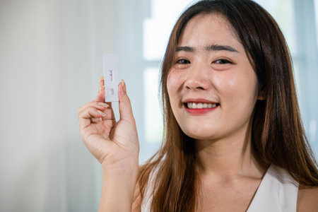 Close up woman showing rapid antigen test kit for selftest with Negative result during swab COVID-19 testing, female holding perform fast coronavirus ATK self test at home in living room, nasalの写真素材
