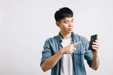 Portrait of a young man isolated over grey, pointing at a calculator number, representing tax day...