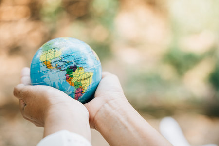 Celebrate World Earth Day with the concept of Green Energy, ESG, and Sustainable Resources. Hold a green leaf and the globe in your hand to signify responsibility and environmental care.の写真素材