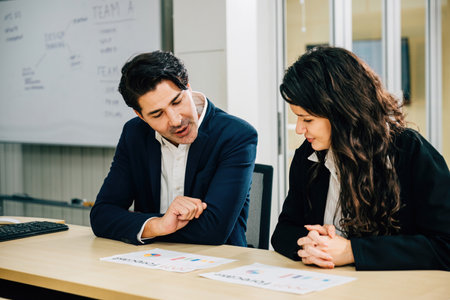 Two businesspeople working together at office desk, engaged in discussion. Their teamwork and...