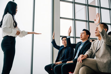 At a conference, a young man raises his hand to ask a question, fostering teamwork and discussion within the group. Active learning and audience engagement are evident.の写真素材