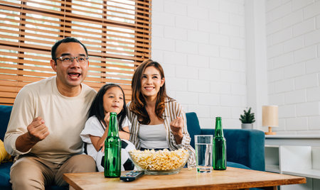 In their cozy living room, a joyful family of fans bond over a football match on TV, celebrating their teams success with cheers and excitement. The room is filled with togetherness and happiness.の写真素材