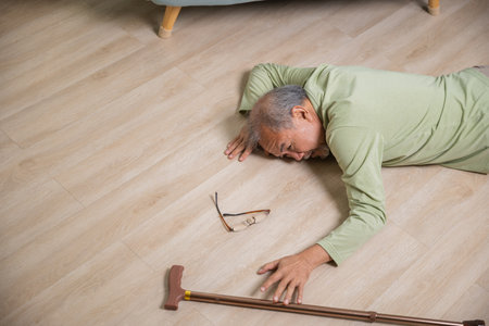 Older senior man headache lying on the floor after falling down he pain and hurt from osteoporosis, Elderly man falling on the floor alone with walking stick at home, Health care and medicineの写真素材