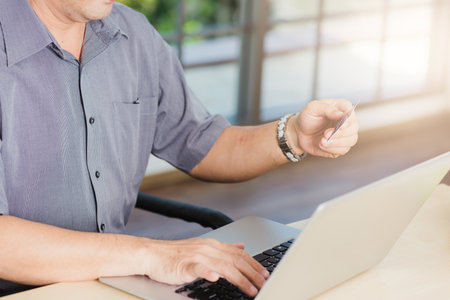 Closeup Asian senior adult man holding credit card and using technology on laptop computer, Online shopping payment with a customer network connection via an Omnichannel systemの写真素材