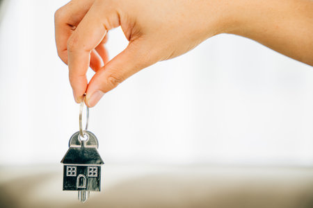 Hand holds house key marking homeowners achievement. Agent presents model home symbolizing real...