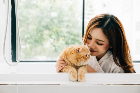 In the bathrooms soothing atmosphere, a woman and her Scottish Fold cat share a bath, a beautiful display of owner-pet love and relaxation.の写真素材