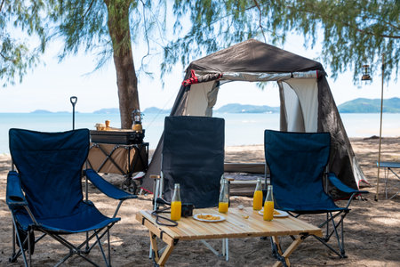 Unwind by the sea, Chairs, picnic table and tent create the perfect camping experience. Sunset, family, and the great outdoors this is where the journey to nature begins. The environment is calling.の写真素材