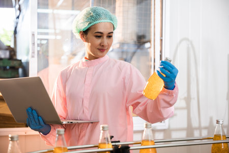 Engineer woman monitors bottles on conveyor belt using laptop in beverage factory. Quality control...