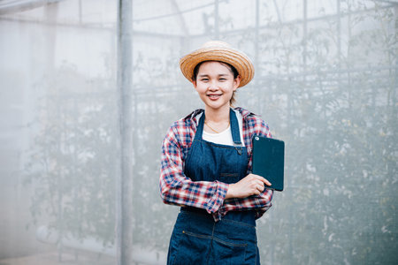 Gardeners, confidently crossed arms, with a tablet at organic tomato greenhouse. Success portrait in futuristic agriculture technology for growth and efficiency.の写真素材