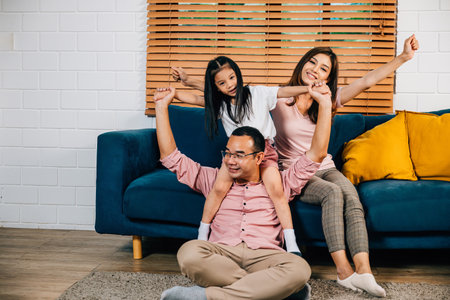 In their modern house an Asian family dad mom and daughter cuddle on a comfortable sofa sharing...
