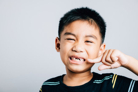 Child an Asian boy highlights dental care by pointing to missing front tooth. White background emphasizes gap and signifies process of tooth exfoliation. Children show teeth new gap, dentist problemsの写真素材
