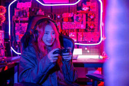 Woman wear gaming headphones playing esports games console gaming room, Gamer using joystick controller for race tournament plays online video game with computer neon lightsの写真素材