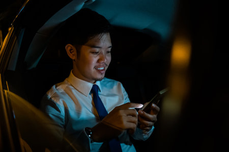 Handsome Asian young man in taxi work on late night sitting back seat and still work with mobile...