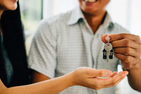 An excited young couple displays keys to their new house celebrating their achievement. Reflecting...