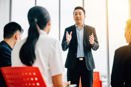 Business professionals from diverse backgrounds work and talk in a modern office. They discuss, present, and brainstorm, underlining teamwork, diversity, and confidence in their meeting.の写真素材