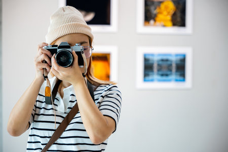Photographer look viewfinder of her camera at front photo frame show exhibit artwork gallery, Asian woman takes picture art gallery collection in framed paintings pictures on white wall with cameraの写真素材