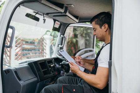 Ethnically diverse mover team in uniform driving a truck for relocation service. Two smiling workers delivering furniture with confidence. Transportation and teamwork showcased. Moving Day Concept.の写真素材