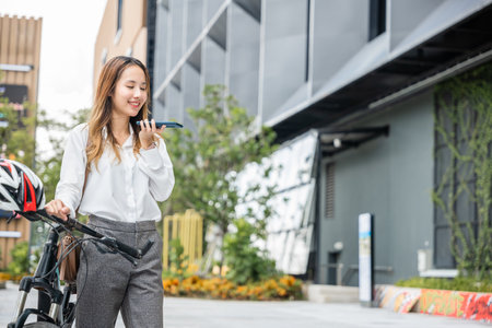 Amid the urban landscape a young woman enjoys a bike ride while staying connected with her smartphone. Her cheerful demeanor reflects the joy of modern freedom and technology.の写真素材