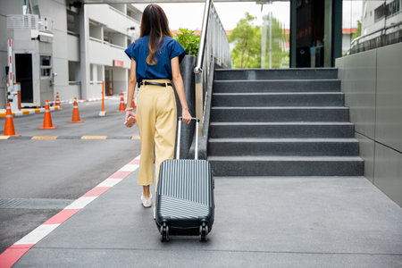 A businesswoman pulling her luggage down a flight of stairs with handrails, ensuring safety and convenience during her journey.の写真素材