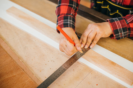 Asian senior woman carpenter taking measurement of a wooden plank and make in workshop, female holding ruler and use pencil drawing sign on plank at woodshop, National Carpenters Dayの写真素材