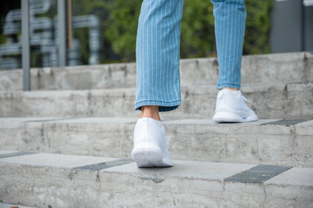 A businesswoman in sneakers conquers the city stairs, symbolizing her determined path. Each step reflects her unwavering progress towards success, highlighting her professional growth. step upの写真素材