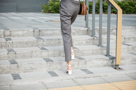A businesswoman in a modern suit is captured in a determined ascent on city stairs. Her black...