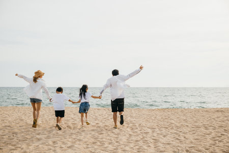 A heartening family scene on the beach parents holding hands running and jumping with their children in holiday laughter. Illustrating the happiness and togetherness of a carefree beach vacation.の写真素材