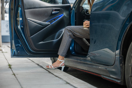 In a city setting a businesswoman in a stylish suit sits in a luxury car. Her slender leg clad in high heels gracefully opens door showcasing the blend of modern transportation and corporate glamour.の写真素材