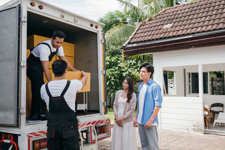 A couple receives professional assistance in moving to their new house. The teamwork of employees is evident as they unload and lift cardboard boxes during the relocation. Moving Day Conceptの写真素材