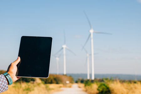 Technician tablet in hand at windmill farm. Engineer ensures clean energy. Expertise in turbine...