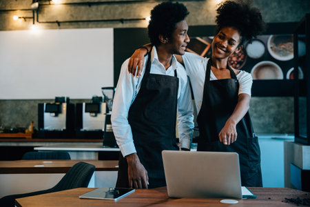 Cafe owners black barista and owner discuss work on laptop in Coffee Shop. Planning supply orders...