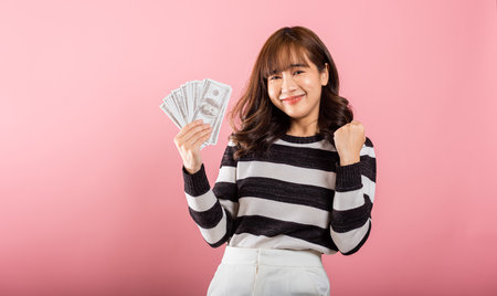 Asian happy portrait beautiful young woman standing smile her celebrating holding dollar money fan...