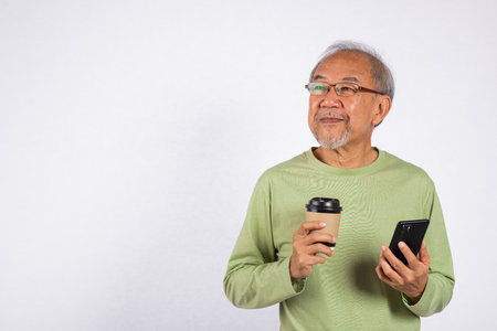 Portrait Asian old man while holding a cell phone and a cup of coffee studio shot isolated on white...