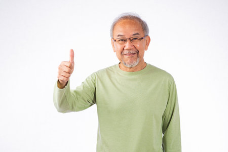 Portrait Asian senior man with glasses and a green shirt is giving a thumbs up studio shot isolated on white background. Concept of approval and positivity, old man smilingの写真素材