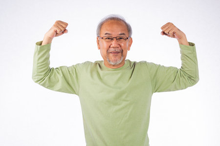 Portrait Asian grey haired smiling senior man flexing muscles and smiling studio shot isolated on white background, elderly showing off very strong and healthyの写真素材