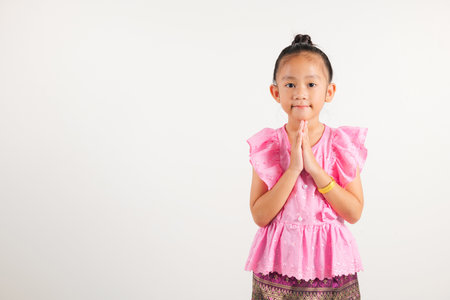Portrait of Thailand kid girl smiling traditional Thai dress costume posing to pay respect in studio shot isolated white background, Happy kindergarten child sawasdee symbol or welcomeの写真素材