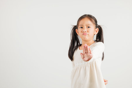 Asian portrait cute young kid girl smiling doing show stop sign gesture with palm of hand but unhappy face studio shot isolated on white background, kindergarten children doubt with copy spaceの写真素材