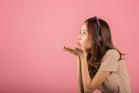 Asian happy portrait beautiful cute young woman teen standing blowing kiss air side something on palm hands expresses her love looking to camera studio shot isolated on pink background with copy spaceの写真素材