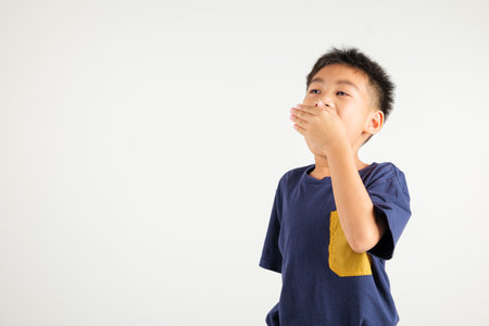Portrait Asian young kid boy emotions tired and sleepy yawning covering mouth open by hand, studio shot isolated on white background, Thai primary child insomnia concept with copy spaceの写真素材