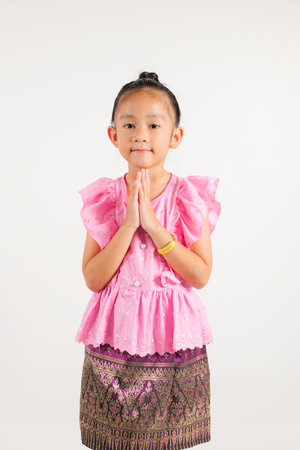 Portrait of Thailand kid girl smiling traditional Thai dress costume posing to pay respect in studio shot isolated white background, Happy kindergarten child sawasdee symbol or welcomeの写真素材